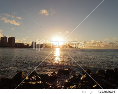 岩場越しに見える夕日の光跡と遠景のダイヤモンドヘッド  133868084