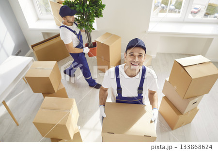 Happy employee of moving service standing in new house holding cardboard box. 133868624
