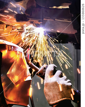 A welder repairs a car's exhaust system, focuses on safety, and uses a burner to cut heated steel in harsh workshop conditions. A welder repairs a car's exhaust system, focuses on safety, and uses a burner to cut heated steel in harsh workshop conditions. 133868626