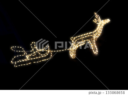 Illuminated reindeer and sleigh display made of warm lights against a dark night sky 133868658