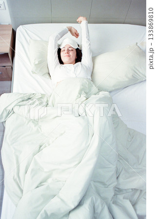 young woman is sleeping, covered with a white blanket and wearing sleep mask over her eyes. 133869810