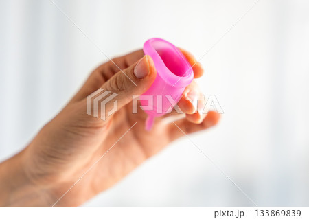 Close-up of a pink menstrual cup standing upright on a woman open palm over wooden table. Feminine hygiene product promoting zero waste, comfort, and sustainable period care. 133869839