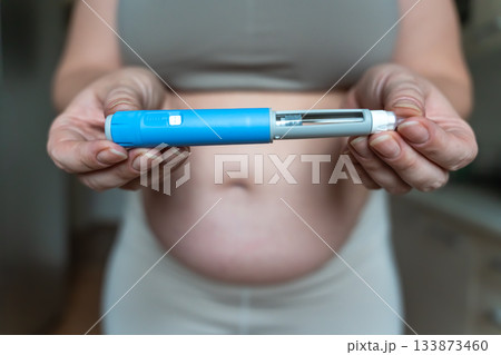 GLP-1 injection pen held by woman in front of abdomen, weight management concept GLP-1 injection pen held by woman in front of abdomen, weight management concept 133873460