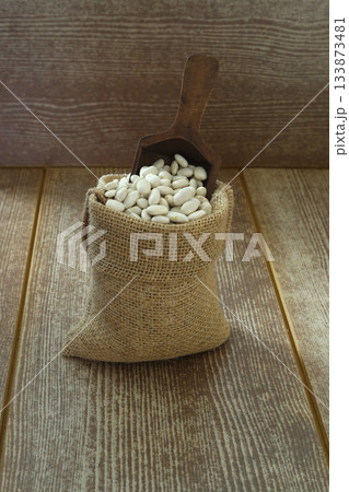 White beans in a bag on a wooden background with space for text. White beans on burlap with wooden spoon White beans in a bag on a wooden background with space for text. White beans on burlap with wooden spoon 133873481