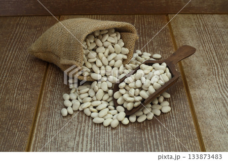 White beans in a bag on a wooden background with space for text. White beans on burlap with wooden spoon White beans in a bag on a wooden background with space for text. White beans on burlap with wooden spoon 133873483