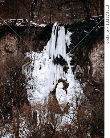 Frozen Waterfall In Bad Urach, Baden Wuerttemberg: Dramatic Winter Ice Formations With Icicles And Snow Covering Rocks And Bare Trees 133873513