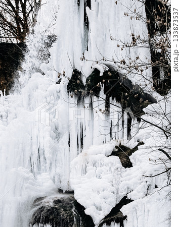 Frozen Waterfall In Bad Urach, Baden Wuerttemberg: Dramatic Winter Ice Formations With Icicles And Snow Covering Rocks And Bare Trees Frozen Waterfall In Bad Urach, Baden Wuerttemberg: Dramatic Winter Ice Formations With Icicles And Snow Covering Rocks And Bare Trees 133873537