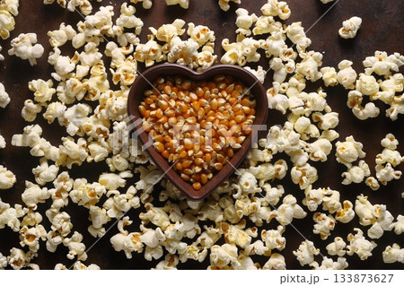 Popcorn in a brown wooden plate in the shape of a heart on a wooden table. 133873627