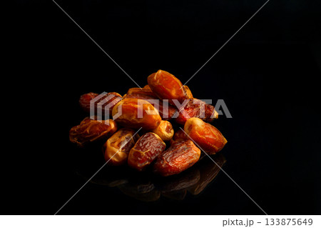 Dates on a black background. Dried fruits. Dried dates lie next to each other Dates on a black background. Dried fruits. Dried dates lie next to each other 133875649