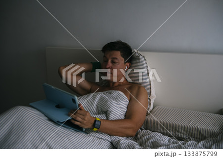 Youthful individual checks device as older person rests peacefully Youthful individual checks device as older person rests peacefully 133875799