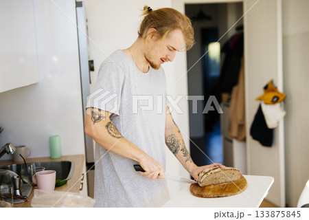 Casual host slices bread on wooden board with gentle light Casual host slices bread on wooden board with gentle light 133875845