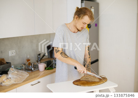 Trimmed for safety, Man cuts sourdough bread amid rustic setting Trimmed for safety, Man cuts sourdough bread amid rustic setting 133875846