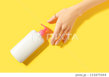 Womans hand holding white bottle on yellow background. Self care concept. 133875944