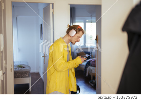 Relaxed individual checking phone amid apartment corridor ambiance Relaxed individual checking phone amid apartment corridor ambiance 133875972