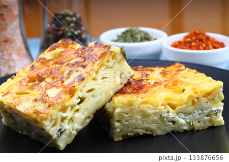 Slices of baked Round Borek cheese pie in kitchen tray with herbs. Dark background. Top view. Copy space Slices of baked Round Borek cheese pie in kitchen tray with herbs. Dark background. Top view. Copy space 133876656