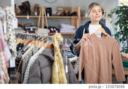 Adult woman chooses warm dress in clothing store Adult woman chooses warm dress in clothing store 133878086