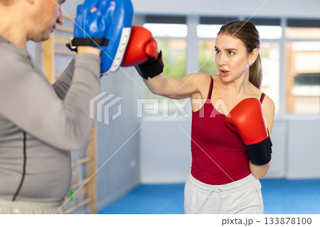 Athletic woman learns to box - hitting punch mitts. Woman with her trainer at gym 133878100