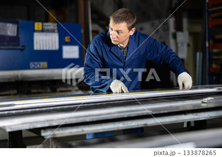 Male worker at metallurgical plant measures an iron sheet using tape measure and marks cutting line Male worker at metallurgical plant measures an iron sheet using tape measure and marks cutting line 133878265