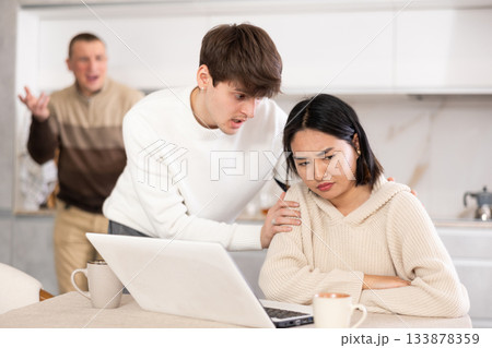 Guy persuades a young girl to stop playing computer games. Upset father in background 133878359