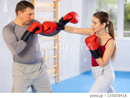 Young girl training boxing kicks on punch mitts held by male instructor 133878418