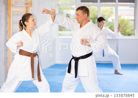 Woman and man in pairs exercising karate movements during group training in gym 133878845