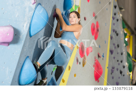 Woman exercising on wall in climbing gym during bouldering training Woman exercising on wall in climbing gym during bouldering training 133879118
