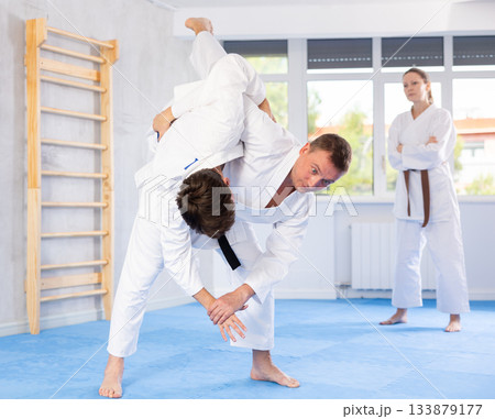 Two males practicing judo together on sports mats under the guidance of trainer 133879177