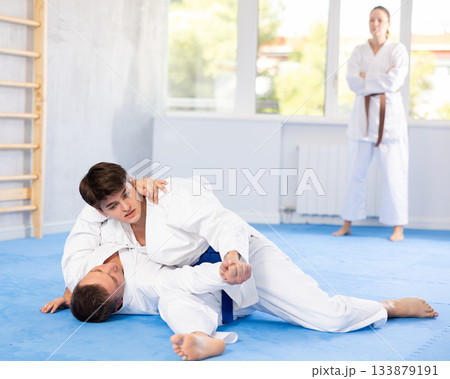 Male athletes in pair conduct training battle in oriental fighting technique under guidance of coach Male athletes in pair conduct training battle in oriental fighting technique under guidance of coach 133879191