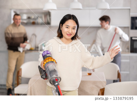Girl vacuuming floor while his relatives help tidy up room Girl vacuuming floor while his relatives help tidy up room 133879195