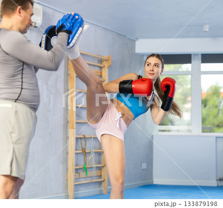 Young girl training boxing kicks on punch mitts held by male instructor Young girl training boxing kicks on punch mitts held by male instructor 133879198