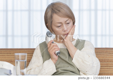 リビングで体温計で体温を測るシニア女性 133880344