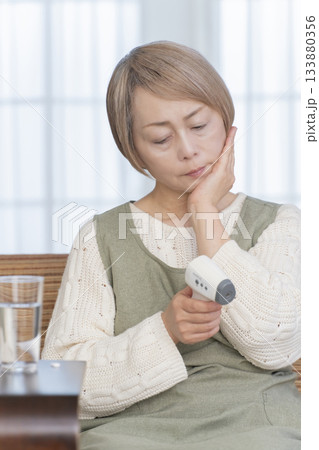 リビングで体温計で体温を測るシニア女性 リビングで体温計で体温を測るシニア女性 133880356