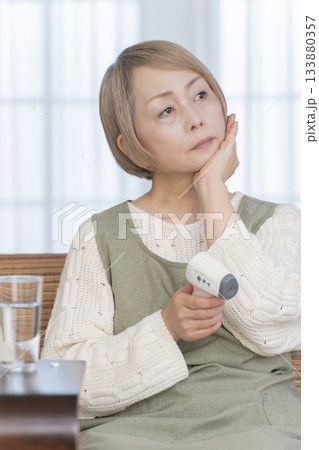 リビングで体温計で体温を測るシニア女性 133880357