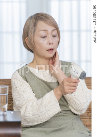 リビングで体温計で体温を測るシニア女性 133880360
