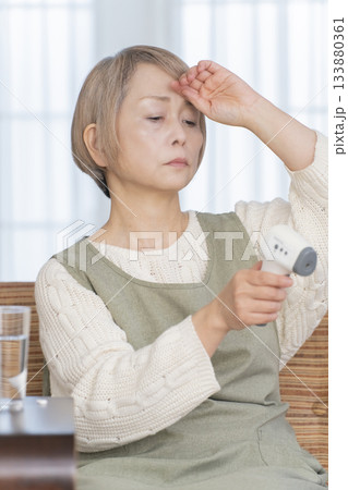 リビングで体温計で体温を測るシニア女性 リビングで体温計で体温を測るシニア女性 133880361