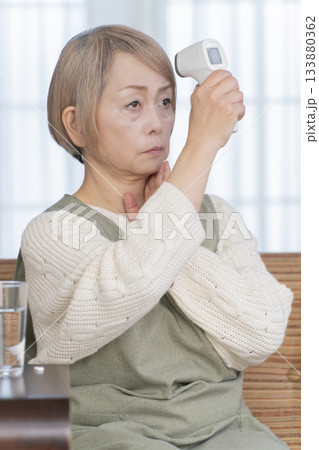 リビングで体温計で体温を測るシニア女性 リビングで体温計で体温を測るシニア女性 133880362