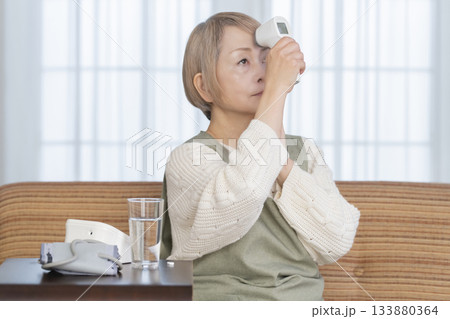 リビングで体温計で体温を測るシニア女性 133880364