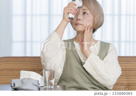 リビングで体温計で体温を測るシニア女性 133880365