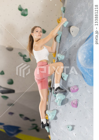 Girl climbs artificial wall bouldering, working out in gym 133881218
