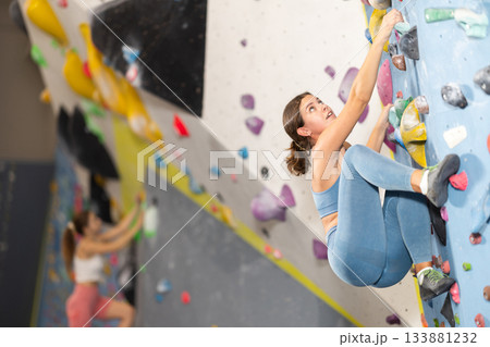 Girl climbs artificial wall bouldering, working out in gym Girl climbs artificial wall bouldering, working out in gym 133881232