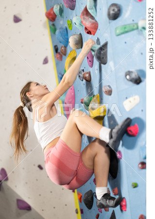Sportive girl climbing on artificial rock wall in rock climbing gym 133881252