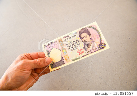 左手で差し出された日本円5000円札の斜め構図 133881557