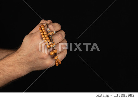 Hands holding wooden prayer beads against a black background 133883992