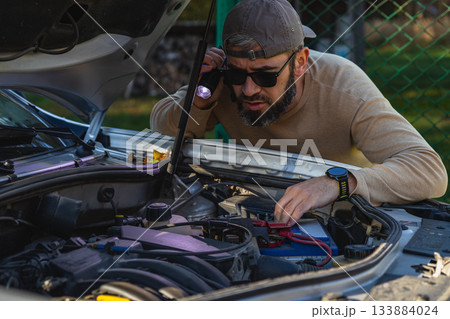 Man repairs car engine in backyard during sunny day 133884024
