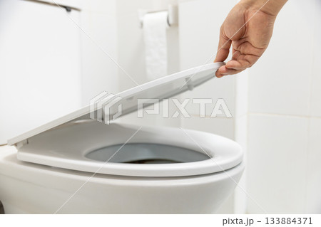 Close up hand is opening the lid of a toilet seat. Close up hand is opening the lid of a toilet seat. 133884371
