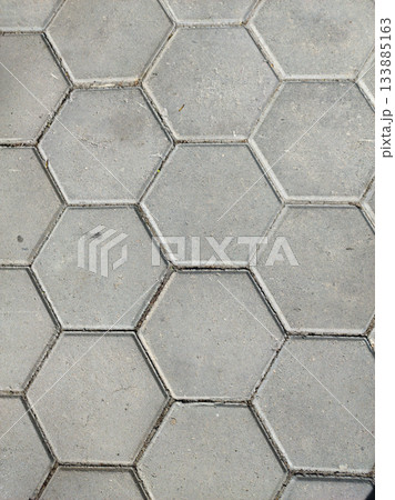 A detailed, top-down view of a textured grey hexagonal paving stone surface. The pattern creates a geometric and uniform background, suitable for construction or design 133885163