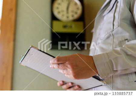 クリップボードを持ち、作業服姿で屋内を点検 133885737