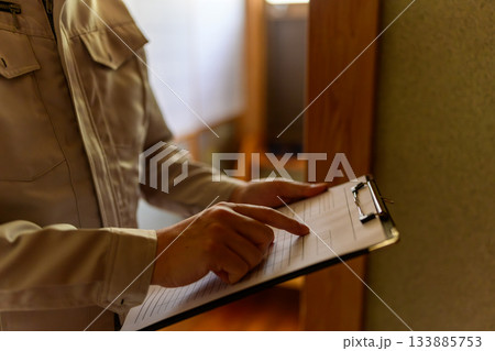 作業服姿の男性がクリップボードの書類を指差して確認する様子 133885753
