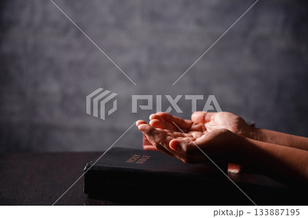 Bible in hand, christian lifts prayer in worship, holding firmly to holy concept of faith, hope and deep belief guides their spiritual life. Hands together in prayer to God along with bible Bible in hand, christian lifts prayer in worship, holding firmly to holy concept of faith, hope and deep belief guides their spiritual life. Hands together in prayer to God along with bible 133887195