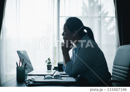 Asian woman sitting at desk with laptop, hands clasped under chin, looking stressed and thoughtful, symbolizing workplace burnout, mental health struggles or silent prayer for hope. Asian woman sitting at desk with laptop, hands clasped under chin, looking stressed and thoughtful, symbolizing workplace burnout, mental health struggles or silent prayer for hope. 133887196